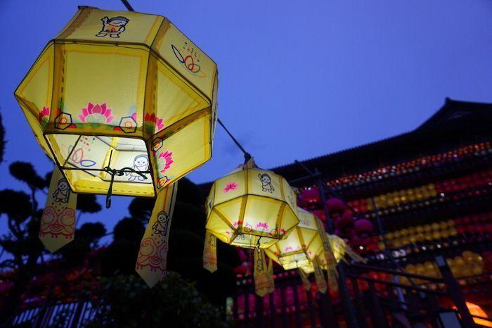Yellow lanterns with traditional Korean motifs glowing at night, captured with a background of beautifully lit temple architecture during a twilight festival.
