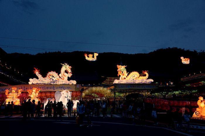 Night view of brightly illuminated dragon lanterns in a Korean cultural festival, with large crowds enjoying the vibrant atmosphere under the evening sky.