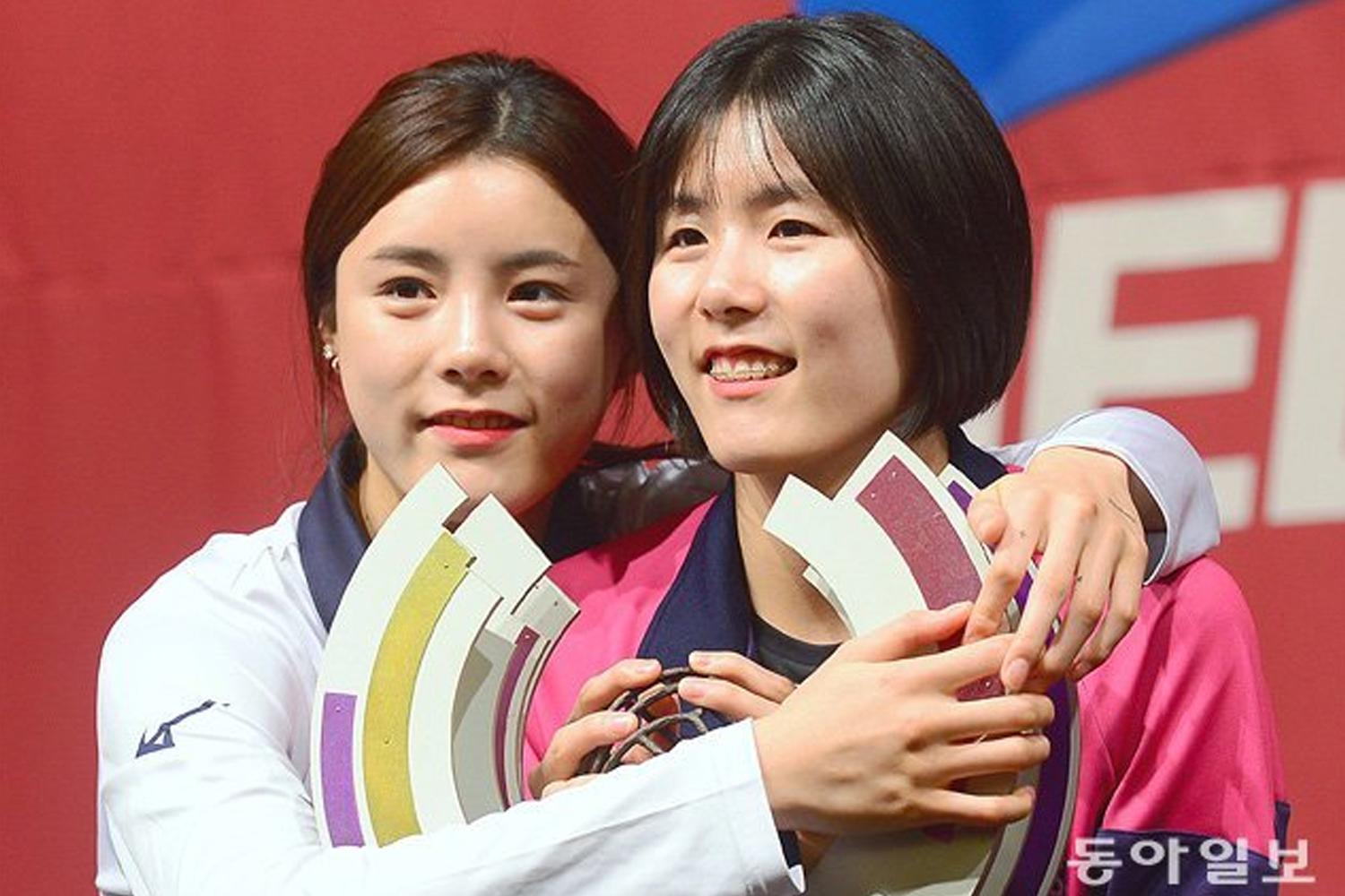 นักกีฬาวอลเลย์บอลในชุดสีชมพูถือโล่รางวัลบนเวทีการแข่งขัน