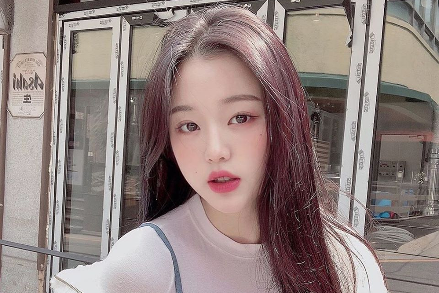 IZ*ONE成員員瑛身披粉色襯衫，背景是充滿了綠色植物和花朵，展現出青春與活力。