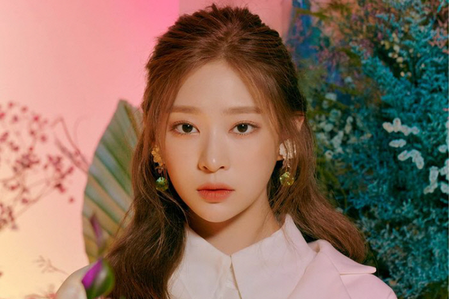 IZ*ONE成員玟周穿著典雅的白色襯衫，背景是粉紅色的柔光幕布，營造出她姿態優雅的形象。