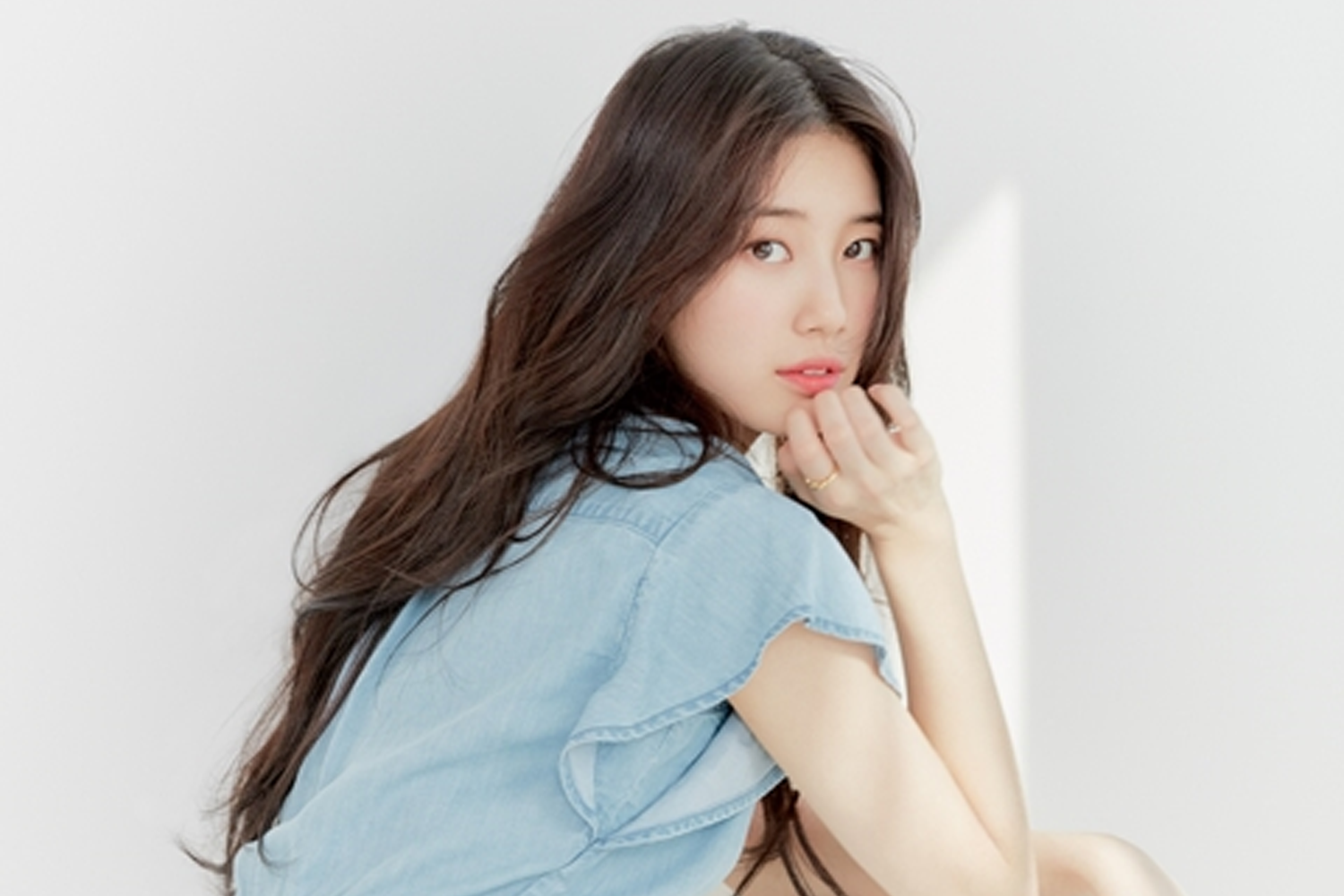 秀智坐在白色背景的柔和光線下，身穿牛仔風格上衣，表達出純真與温柔的魅力。