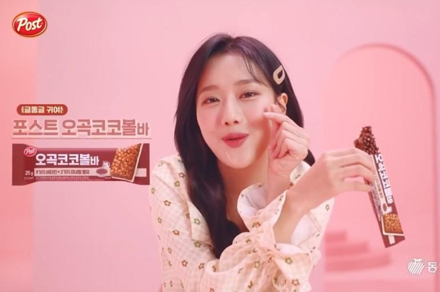 一位模特手持東西食品巧克力棒的廣告形象，背景是粉紅色調，巧克力棒的包裝在畫面左上角展示。