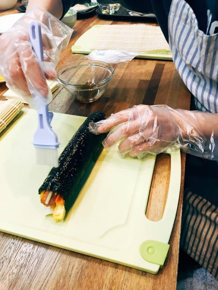 A person applying sesame oil on rolled kimbap with a brush.