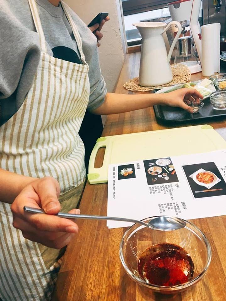 Cooking participant stirring ingredients for spicy stir-fried rice cakes with a spoon in a bowl.