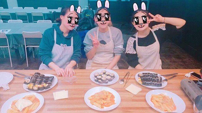 Participants at a Korean cooking class proudly displaying their kimbap and tteokbokki preparations.