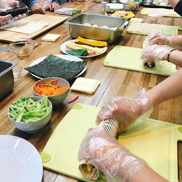 Participant rolling Korean kimbap with a bamboo mat on a preparation counter.