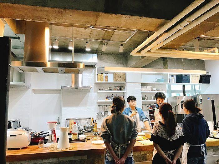 Cooking school participants gathered around a kitchen counter, listening to instructions.