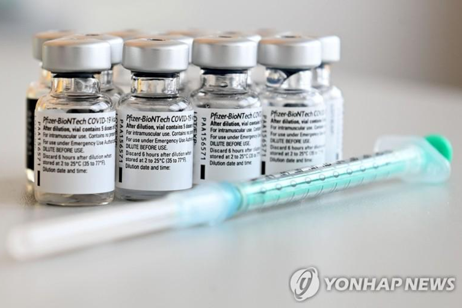 多瓶輝瑞BioNTech COVID-19 疫苗在白色背景上展示，旁邊擺放著一支針筒，來源: Yonhap News