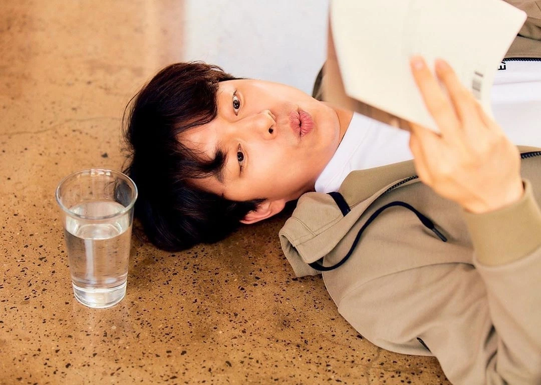 在温暖厨房地板上躺卧的孔刘，手持一本打开的书，塑造出一种闲适与智慧共存的画面。