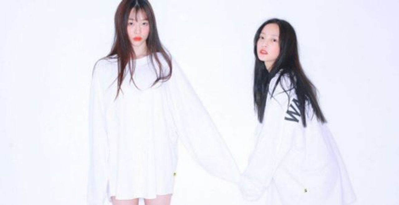 兩位穿著寬鬆白色衣服的女性，手持手相互給予支持。