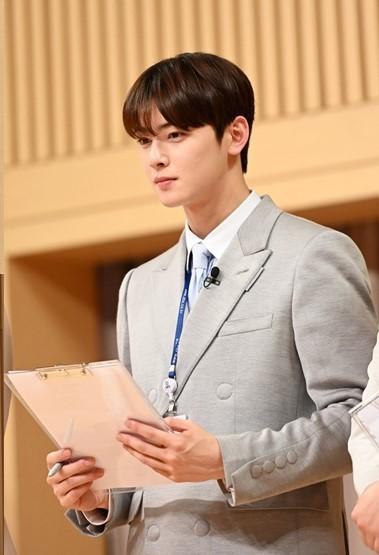 グレーのダブルボタンのスーツを着た男性、韓国アイドルのASTROメンバー、クリップボードを持ち、室内での姿。