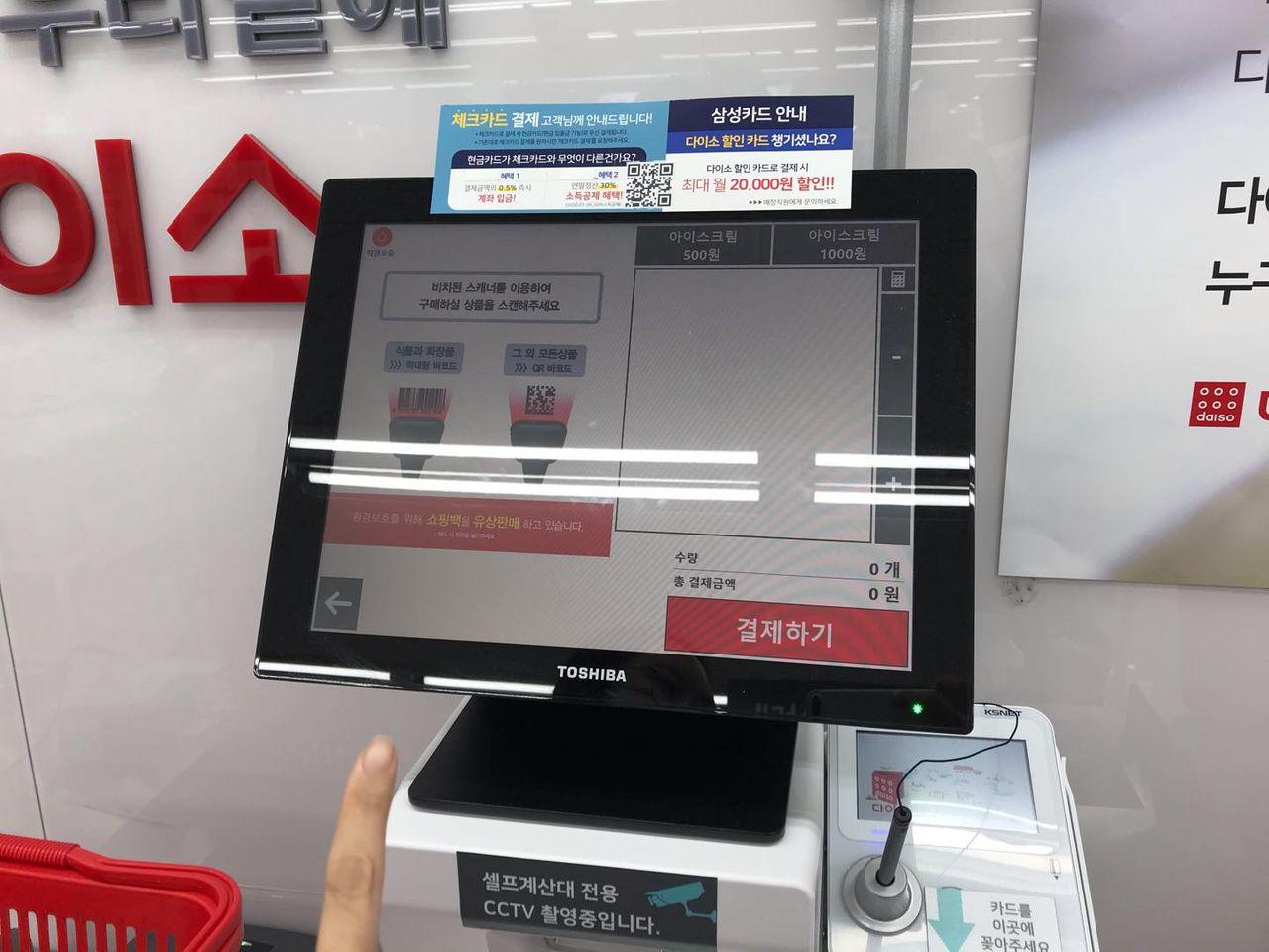 ผู้ใช้งานกำลังใช้บาร์โค้ดสแกนเนอร์ในการสแกนสินค้าในร้านไดโซะเพื่อทำการชำระสินค้าผ่านเครื่องจ่ายเงินอัตโนมัติ