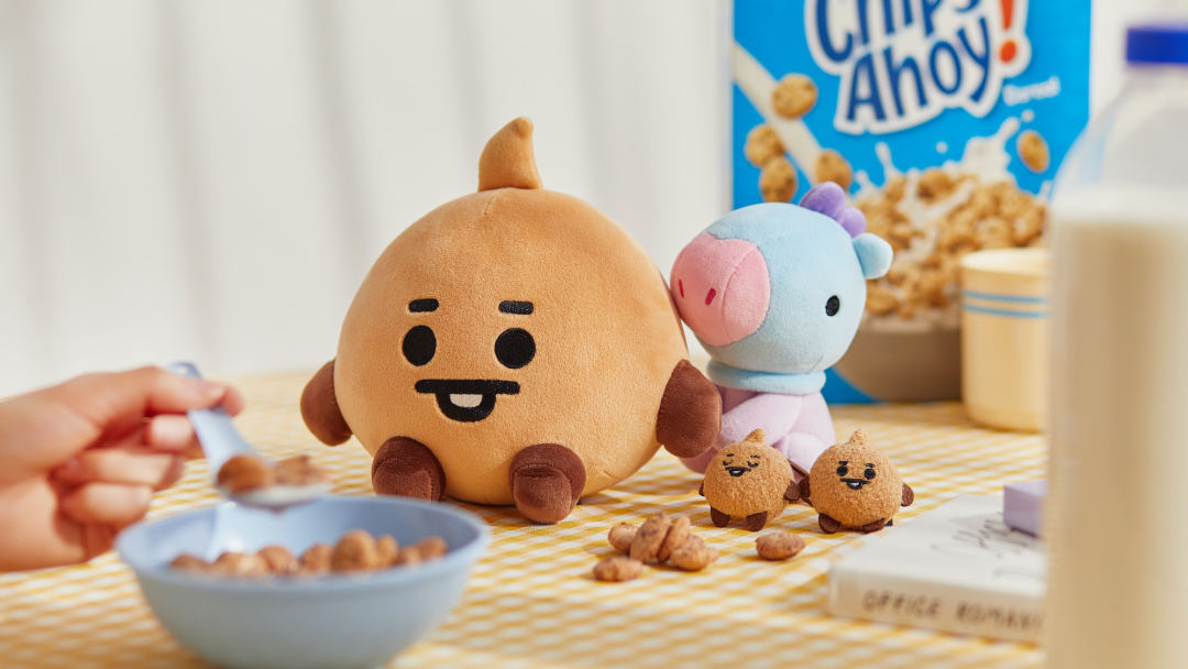 BT21玩偶RJ和MANG享受早餐场景，桌上有牛奶和谷物盒。这一可爱的组合展示了一种和谐与快乐的生活方式。