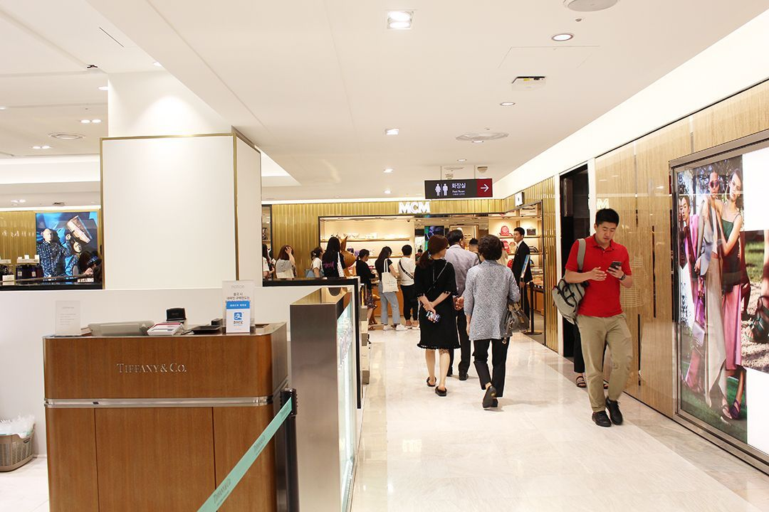 樂天免税店室內購物區，顧客在享受多樣商品選擇和購物體驗，背景顯示品牌專櫃區域。