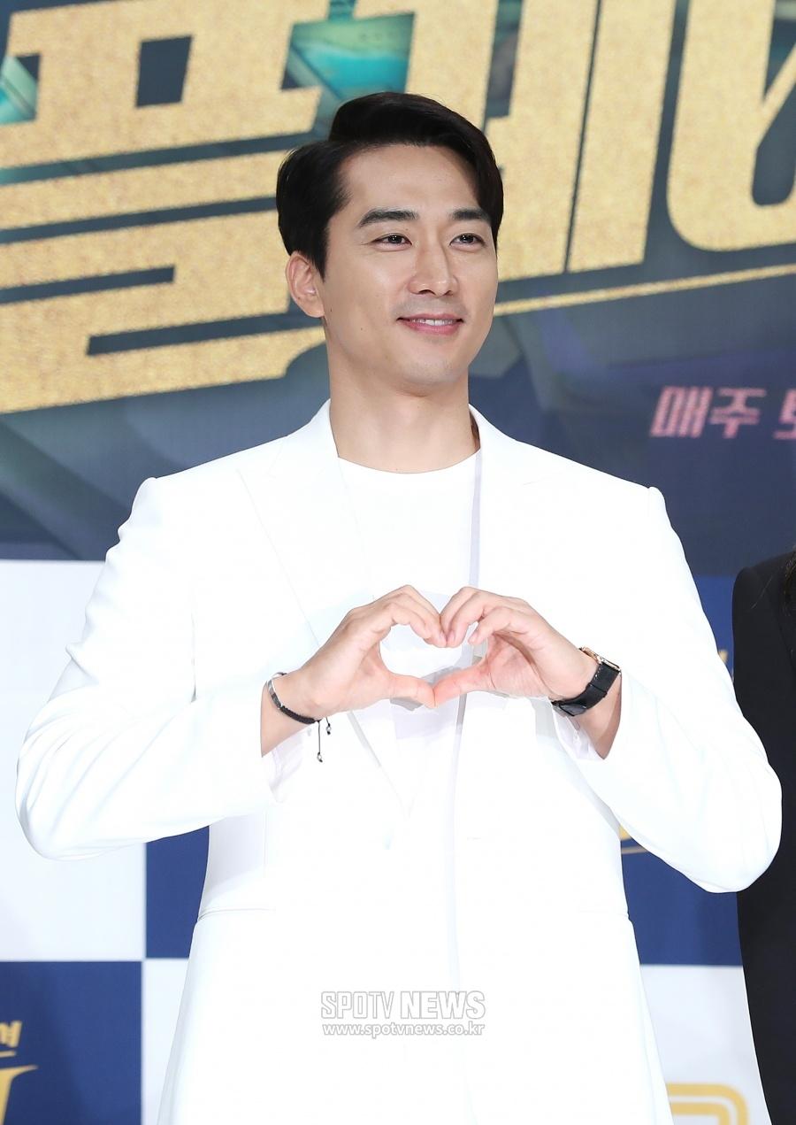韓国の俳優ソン・スンホンがハートのジェスチャーをする姿。彼のフレンドリーで愛らしい一面を表している。
