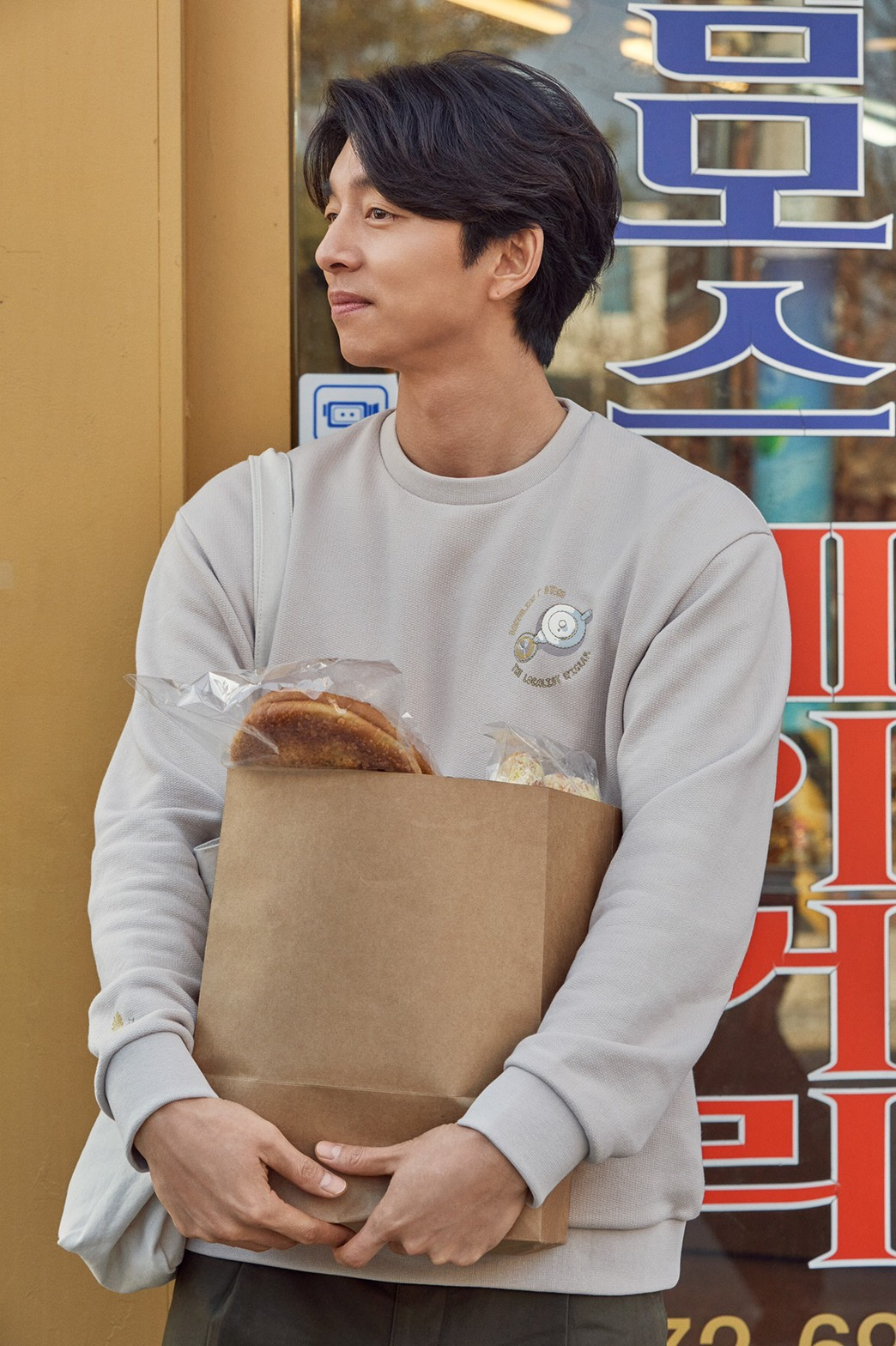 穿着柔和色调毛衣的孔刘，手持购物袋站立在店门口，展现生活方式与时尚装扮的完美结合。