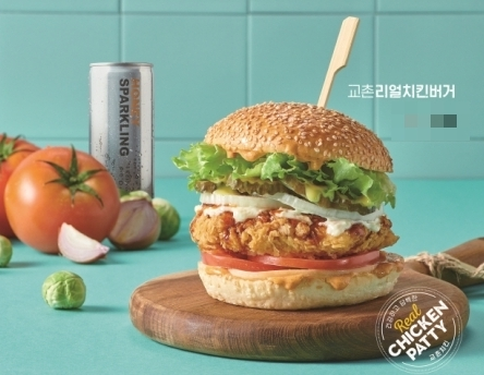 內有炸雞肉排、萵苣、番茄、特製哇嗚醬的韓國橋村炸雞Real炸雞漢堡照片，背景是綠色磚牆