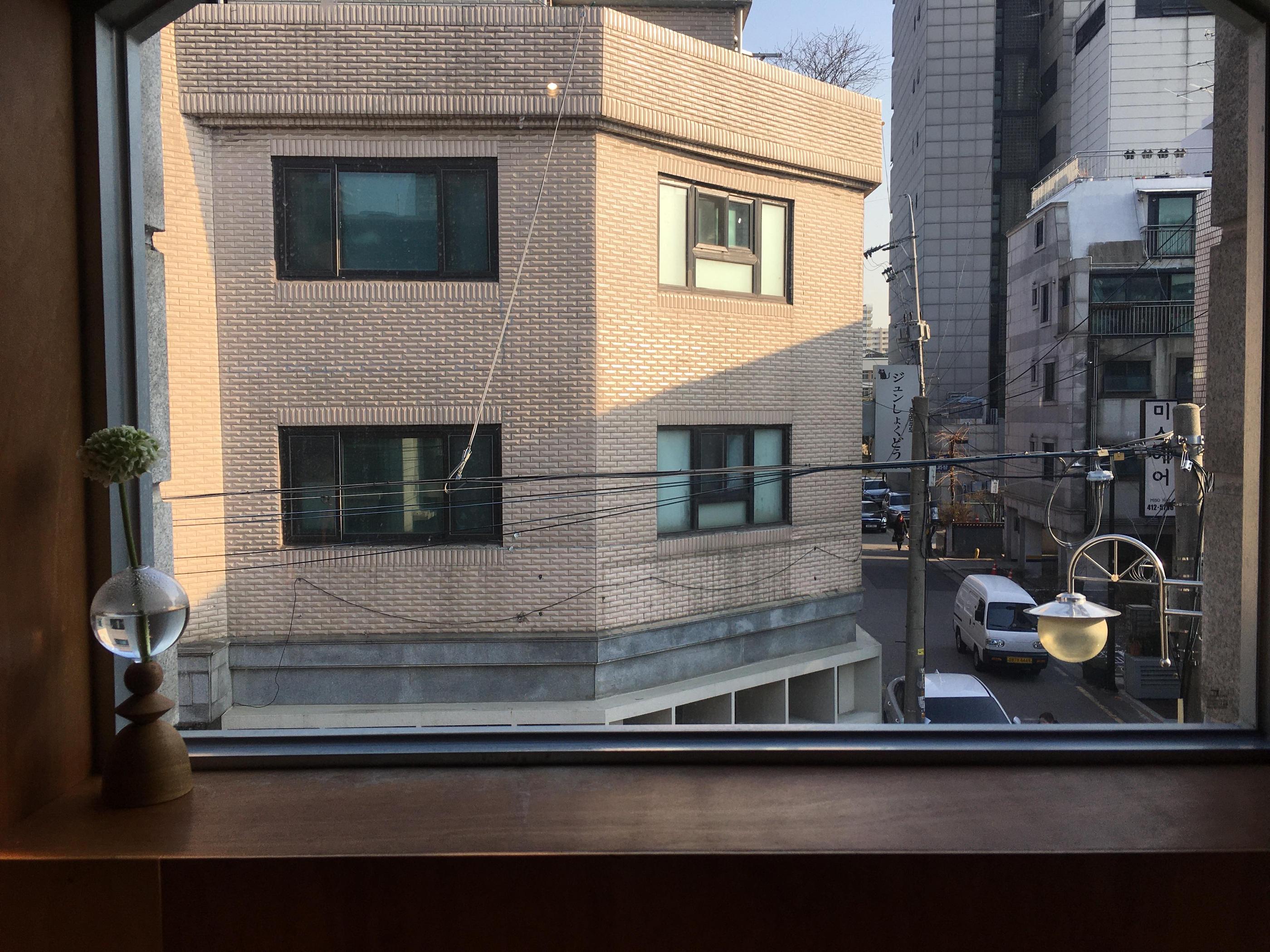 Cửa sổ với tầm nhìn toàn cảnh đường phố Seoul, kết hợp với cây xanh và đồ trang trí nhỏ tạo cảm giác hoài cổ và ấm áp.