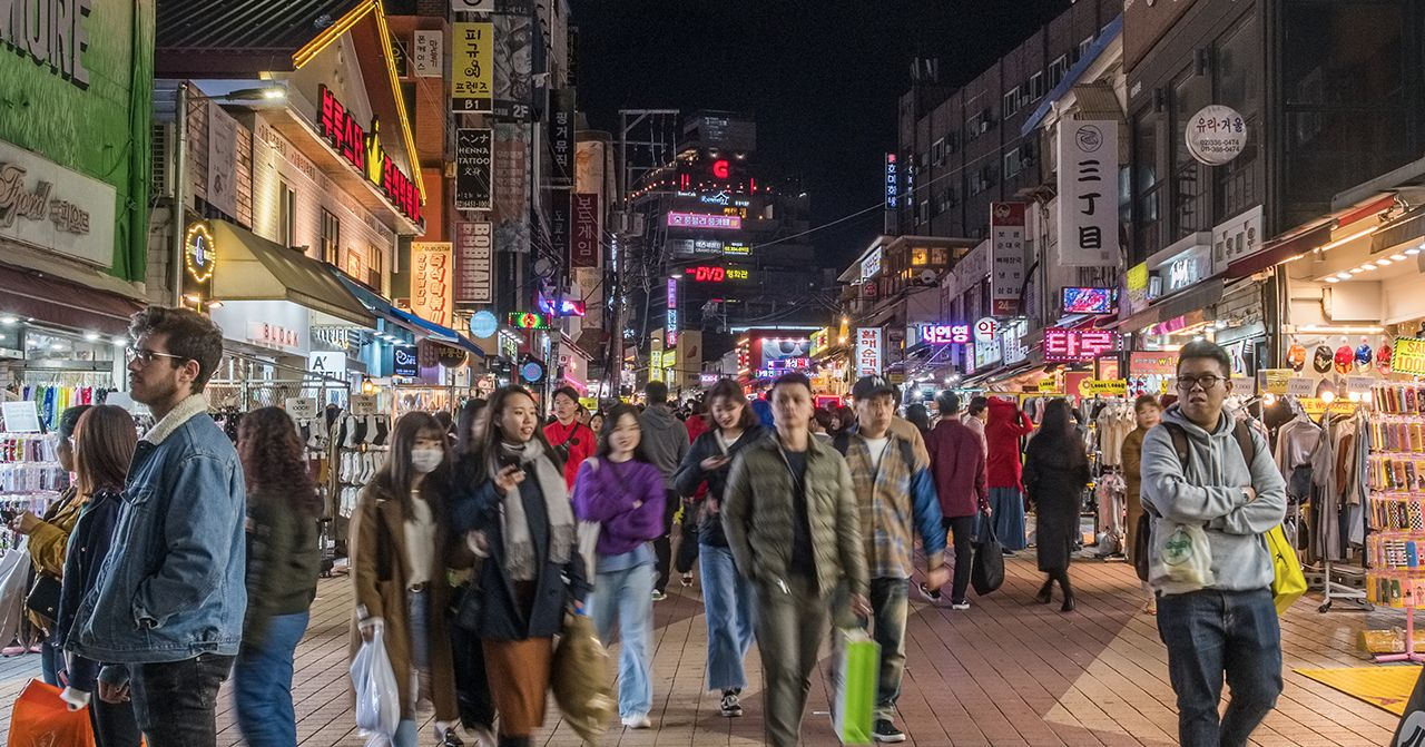 ถนนในย่านช้อปปิ้งที่เต็มไปด้วยผู้คนและร้านค้าที่มีป้ายไฟแสงสว่างในตอนกลางคืน