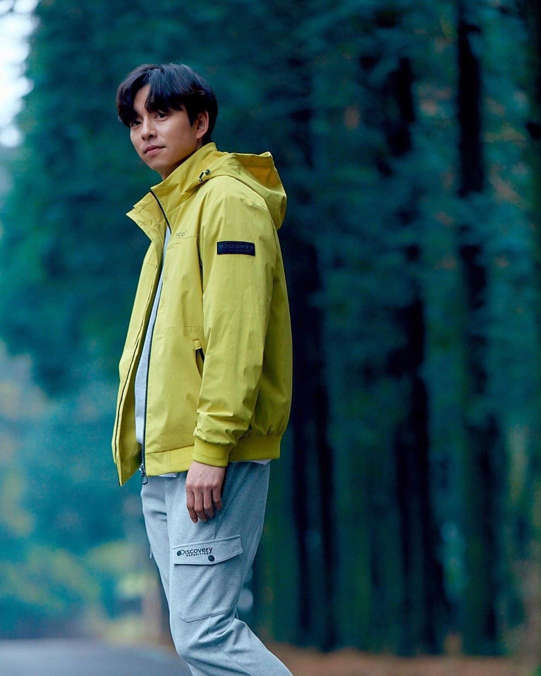 低角度拍摄视角，看向远方的孔刘，身穿Discovery黄绿色夹克，展示其活力和探索精神。
