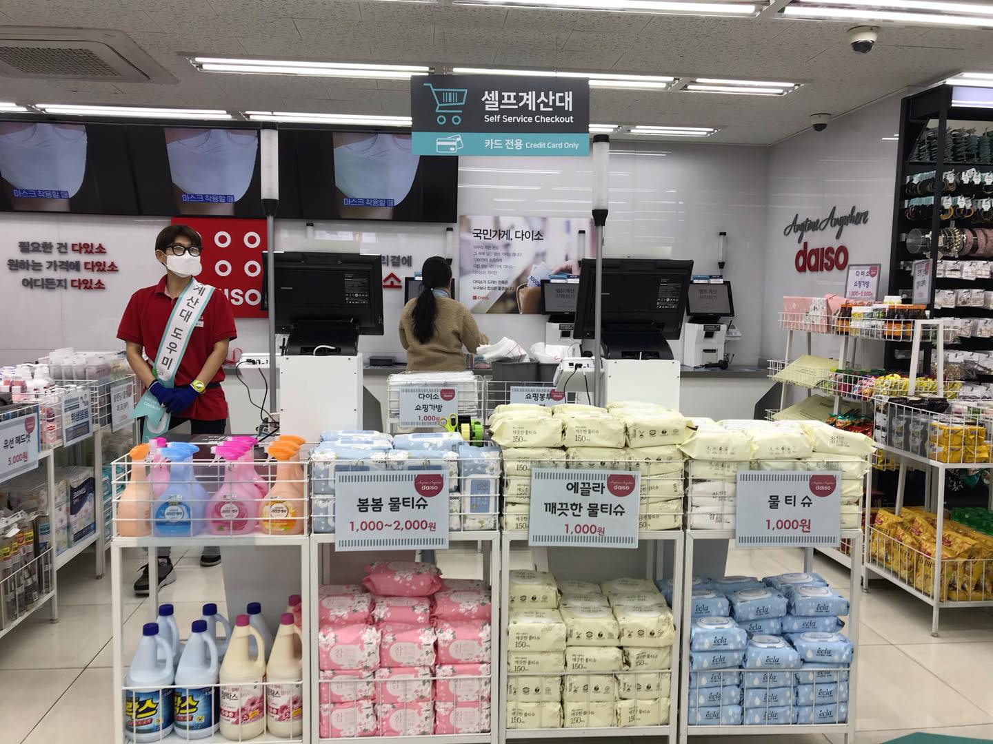ภาพภายในร้านไดโซะในเกาหลีแสดงส่วนเครื่องจ่ายเงินอัตโนมัติพร้อมป้ายภาษาเกาหลีบอกว่าเป็น 'เซลฟ์ เซอร์วิส แคชเชียร์' และสินค้าที่วางอยู่ข้างหน้าเครื่องจ่ายเงินอัตโนมัติที่ลูกค้าสามารถเลือกซื้อได้ในราคาประหยัด