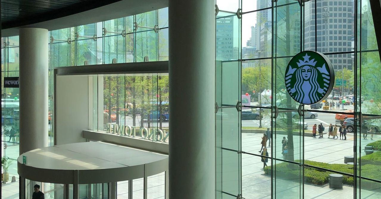 韓國某星巴克分店的大樓入口，展示了城市的現代化景色和星巴克品牌的標誌，強調了大企業的安全措施。