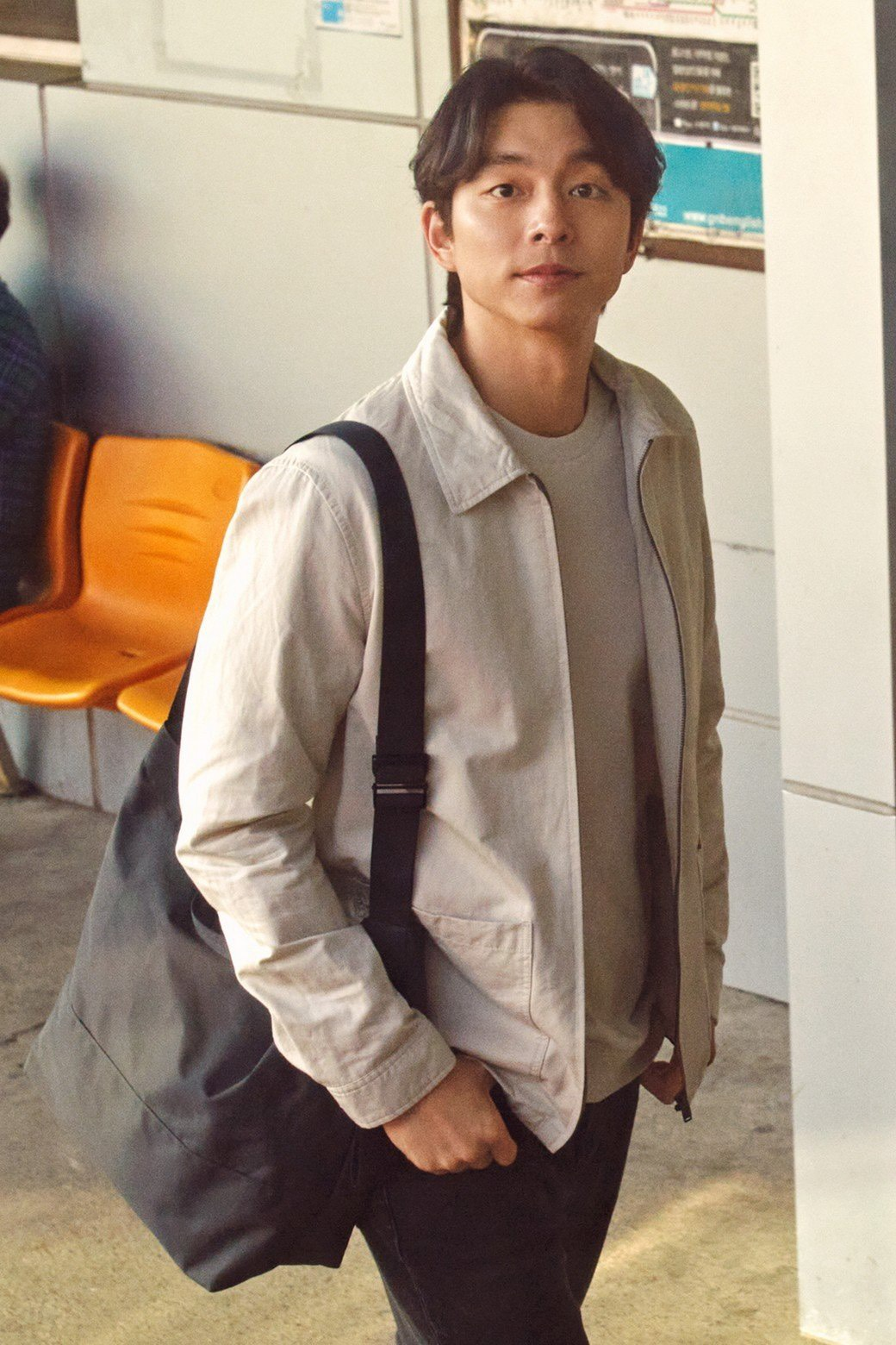 身穿浅色夹克，搭配米色背包，孔刘在交通站台旁休闲漫步，突显旅行与日常风格的完美融合。