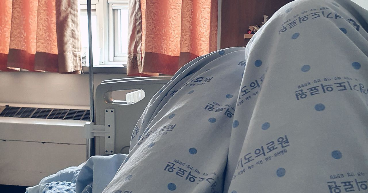 病房內景，患者躺在病牀上，房間窗户讓光線進入，給人以沉靜的感覺。