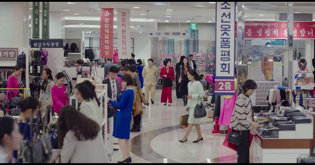 北韩百货商店的内部景象，展示了不同商品和穿着多样的顾客 - 展现日常生活的商业环境