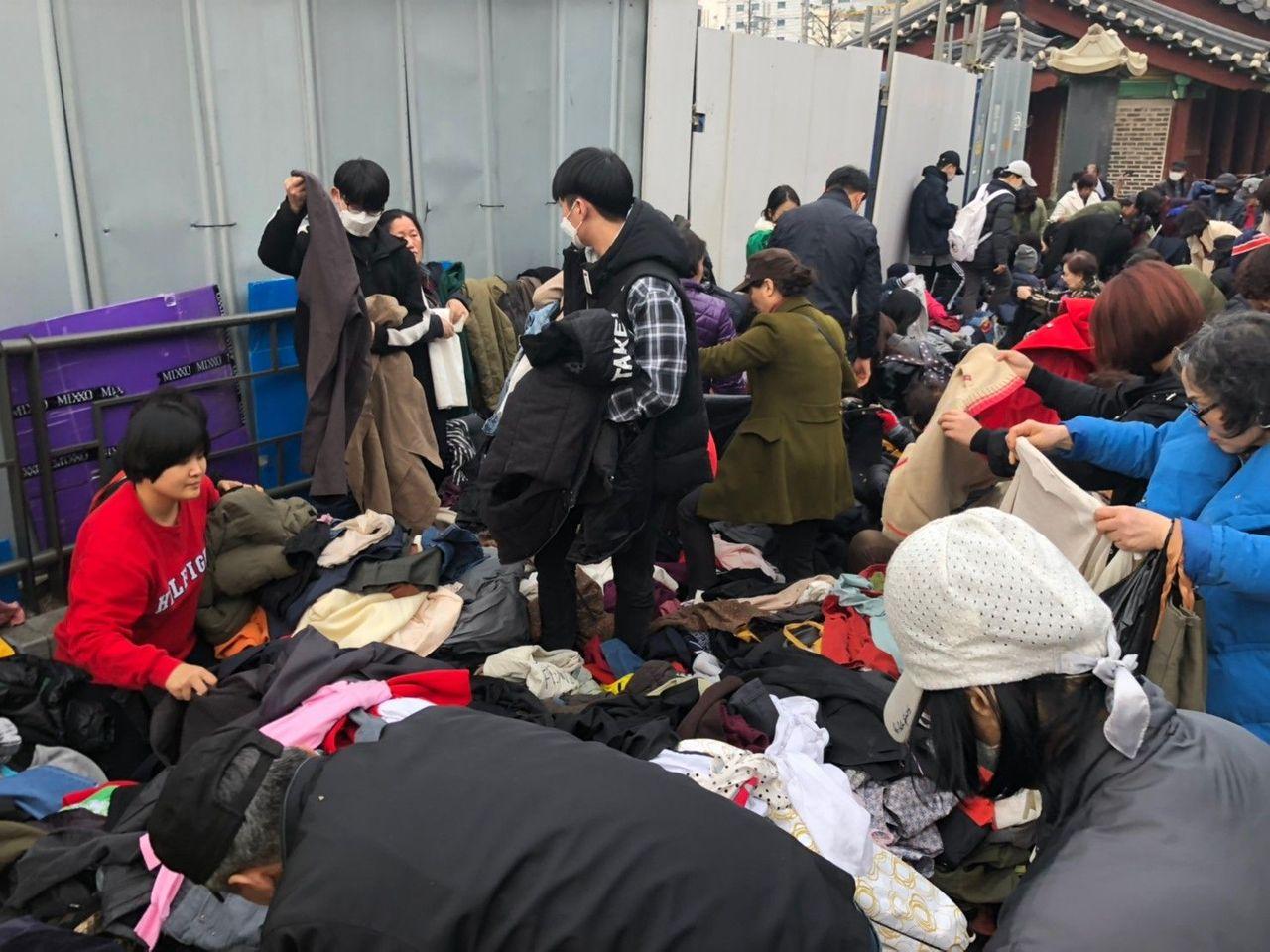 ภาพของผู้คนกำลังเลือกซื้อเสื้อผ้ามือสองจากกองเสื้อผ้าในตลาดนัดดงมโย โซล