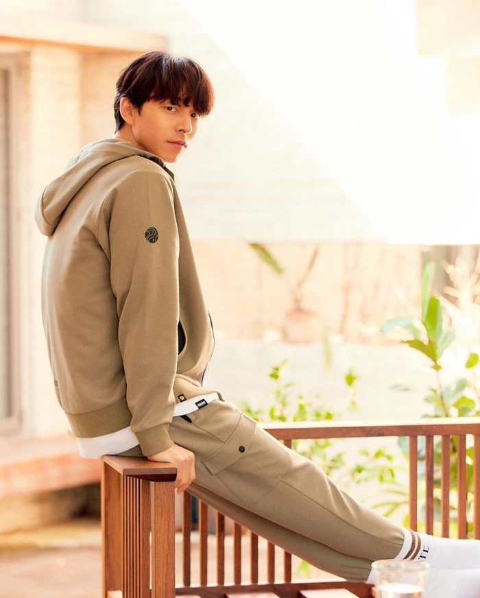 身穿Discovery品牌套装的孔刘，坐在室外长椅上，灿烂阳光洒在他微微微笑的侧脸上。