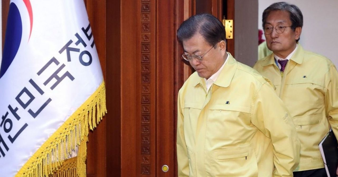 南韓政府官員在會議後發表防疫措施的相片，政府旗幟旁的官員穿著黃色夾克。