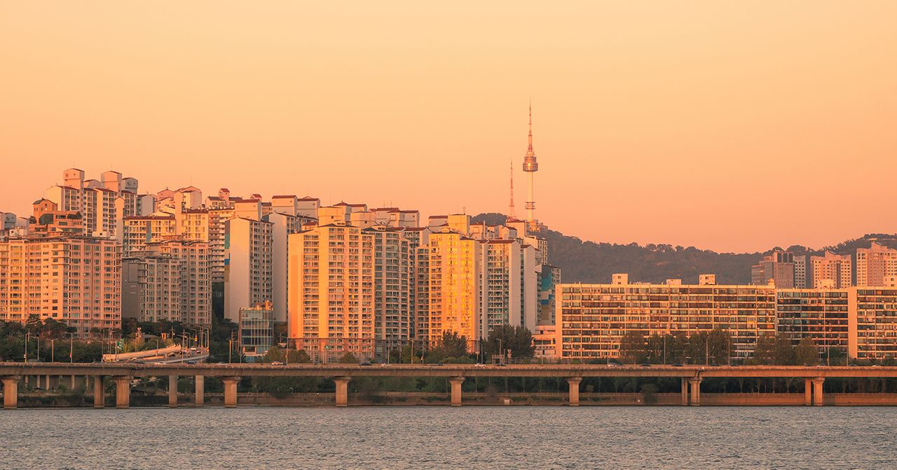 在日落時刻，首爾城市天際線綻放著柔和的橙金色光芒，呈現出當地獨特的都市景觀，遠處可見南山塔的身影。