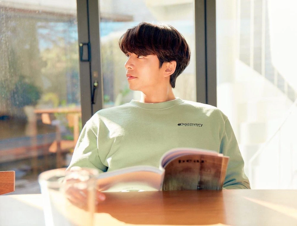 身穿Discovery品牌卫衣的孔刘，坐在开放式客厅中，流露出一种放松而又专注的氛围。