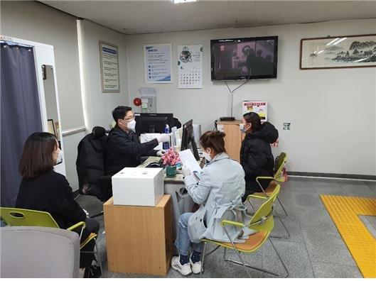 群山市の事務所内で、マスクを着用した数名の人々が椅子に座り書類を持っている様子