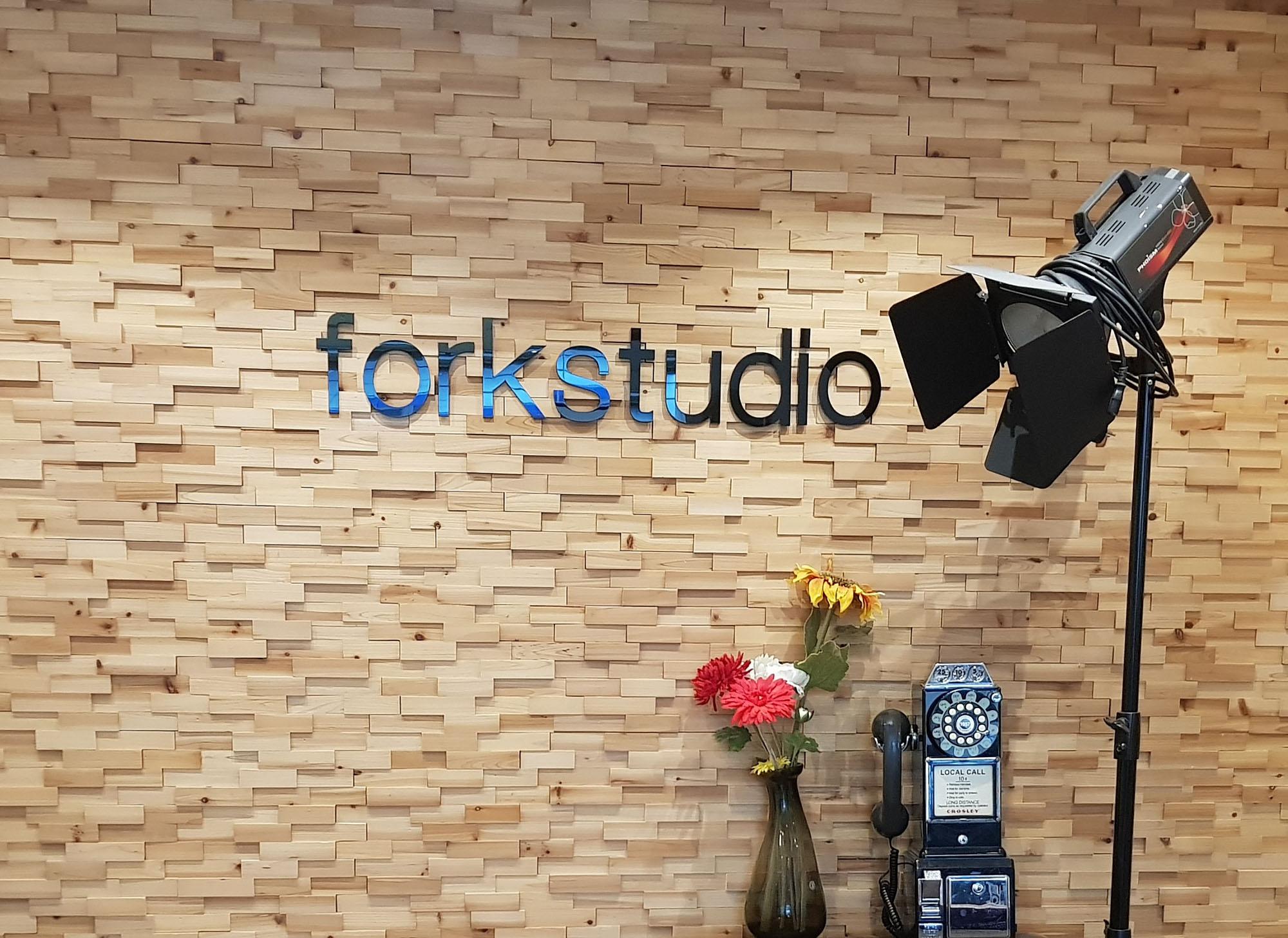 Indoor studio with brick wall, wooden accents, plants, and flowerpots. A photograph, vase, and typography add decorative touches.
