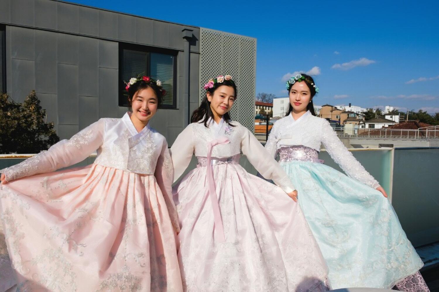 A woman in pink Korean gown smiles at the camera, standing in front of the beautiful skyline of Gyeongbokgung Palace.