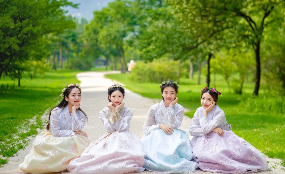 Happy tourists in Gyeongbokgung hanbok rental shop wearing traditional Korean clothing, posing in front of lush greenery.