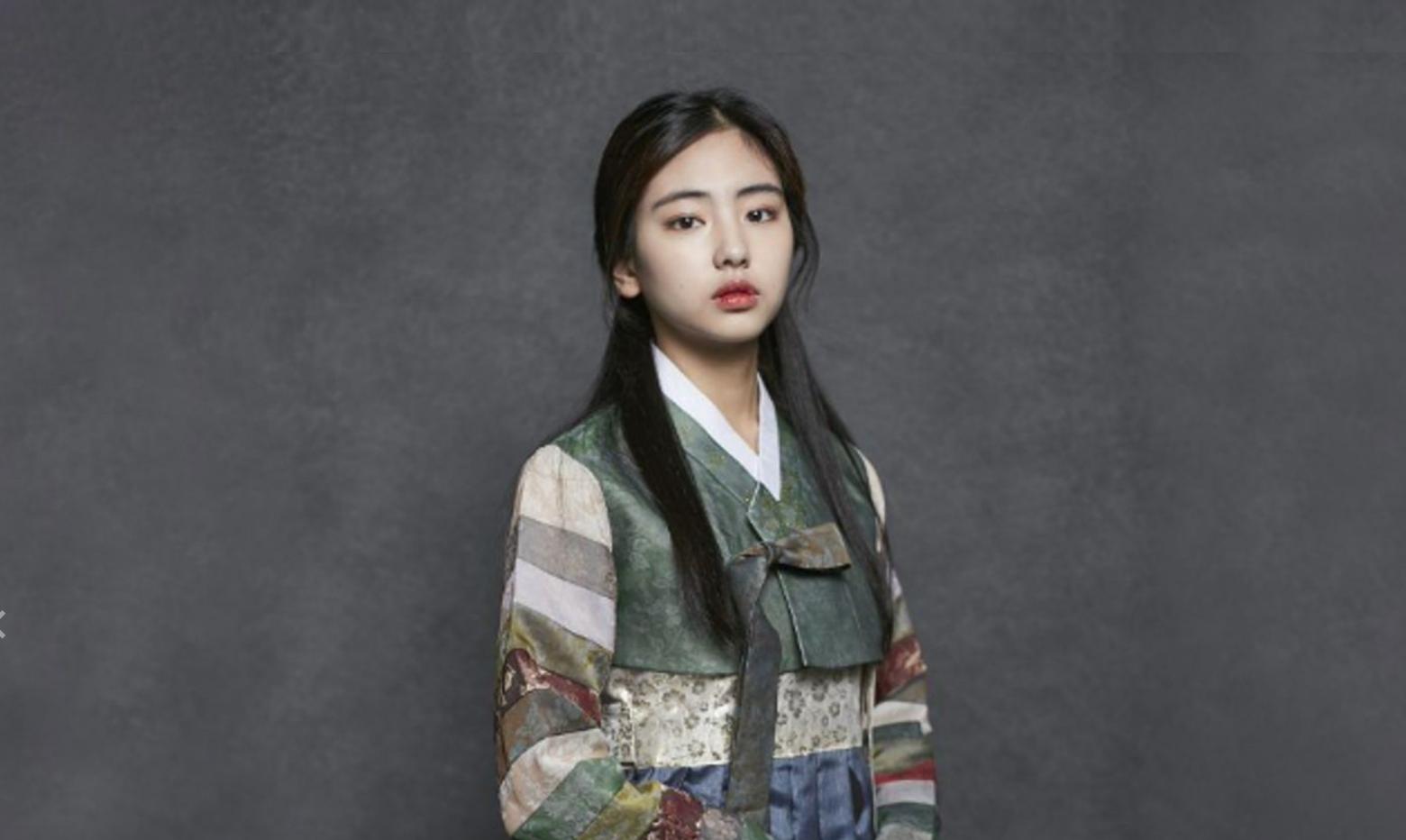 Hanbok-clad model wearing black hair, lip color and jewelry poses with a gesture at Gyeongbokgung rental shop.