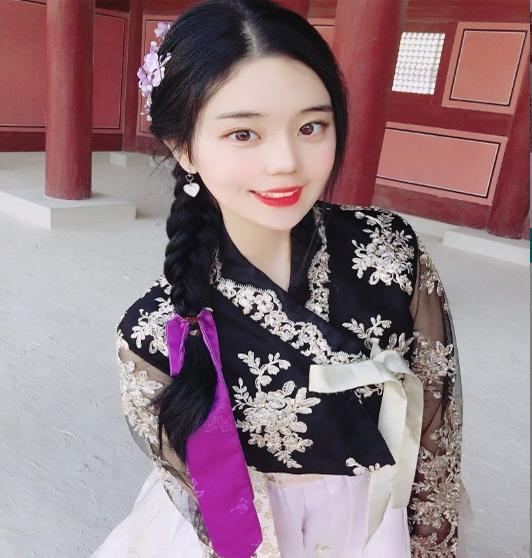 Smiling girl in magenta hanbok at Gyeongbokgung Palace, with bold makeup and black hair, standing confidently with hands on waist.
