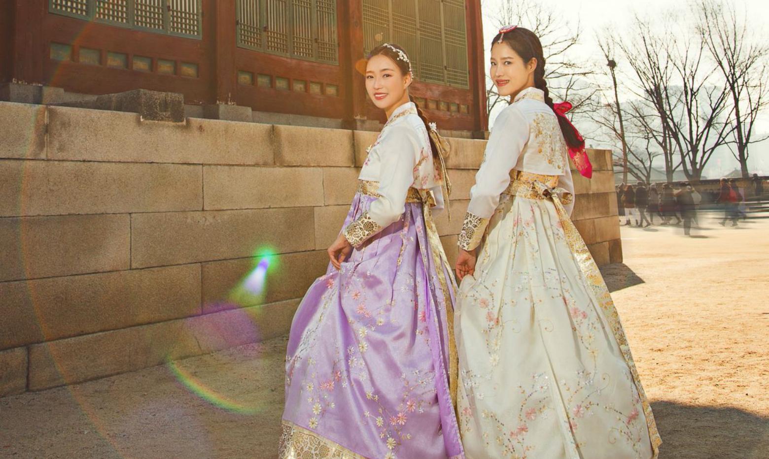 smiling women wearing pink and magenta hanbok, standing in front of a traditional building at 경복궁. Enjoying leisure time in traditional Korean fashion design from 예스한복.