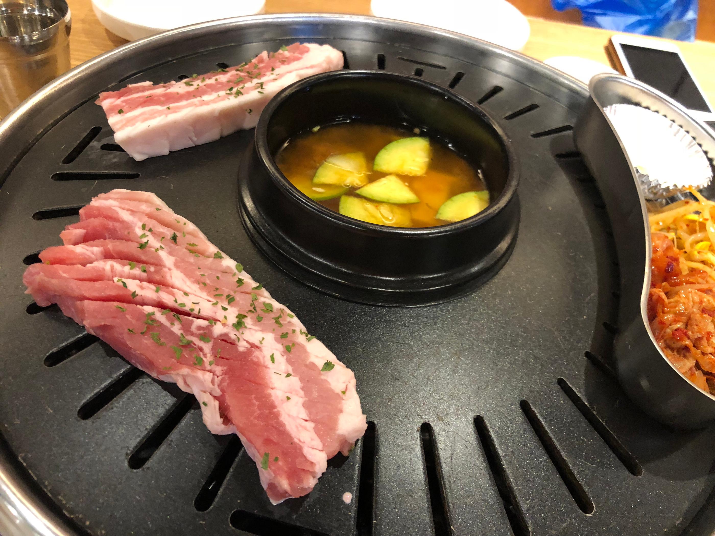 Delicious pork dish being cooked on frying pan with tableware and ingredients at Korean restaurant in Seoul.