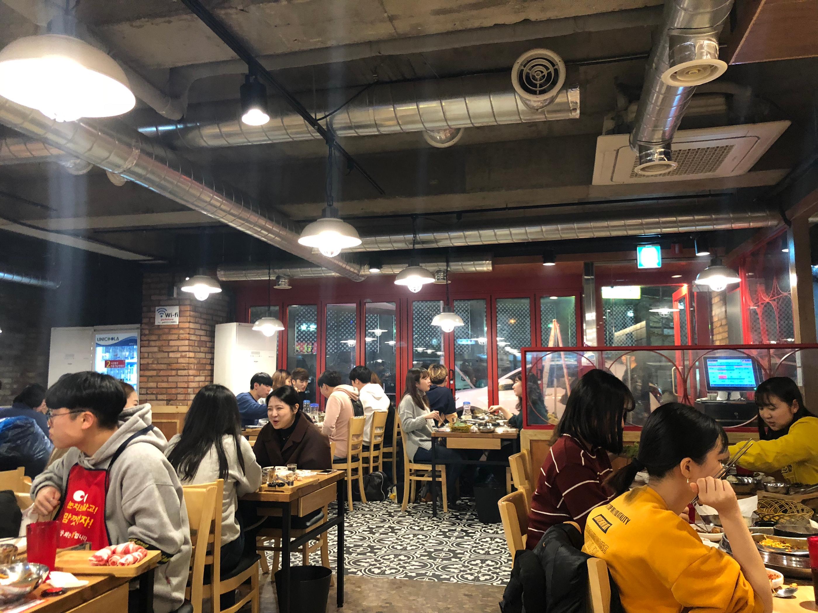 Interior of Gangnam Dwaeji Sanghoe with customers seated at tables and chairs for unlimited refill event.