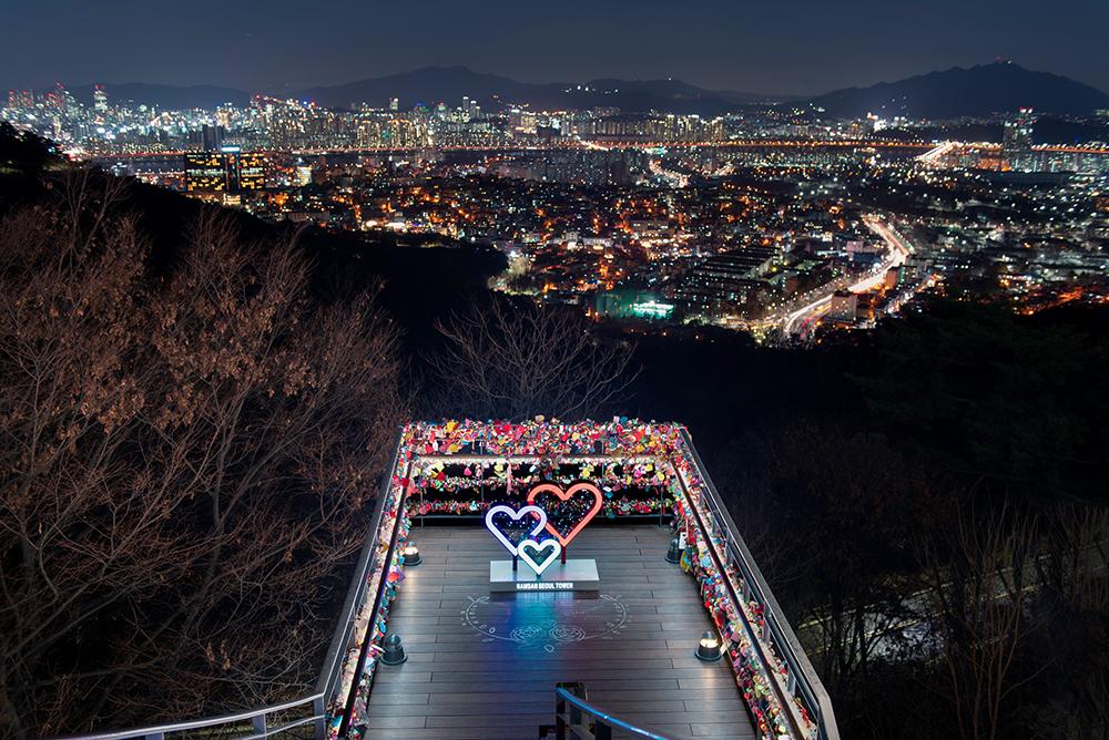 View from N Seoul Tower overlooking city skyline, bridge, and natural landscape.