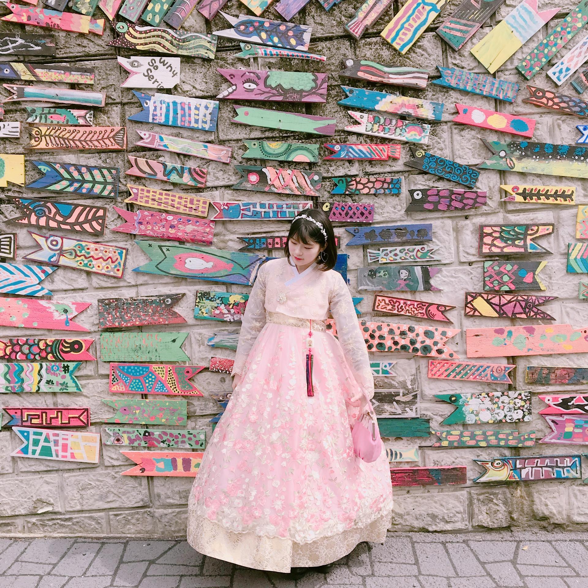 A pink 한복 dress for rent at a clothing shop in Busan. The dress has traditional 한복 sleeves and is shown in a temple. Textile and fashion photography.