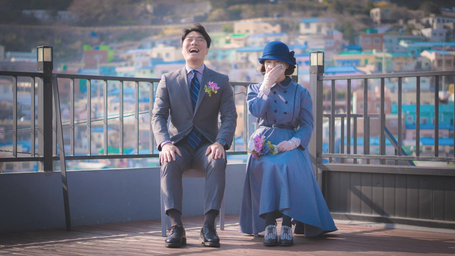 Smiling man and woman wearing modern Korean clothing, posing for flash photography. 