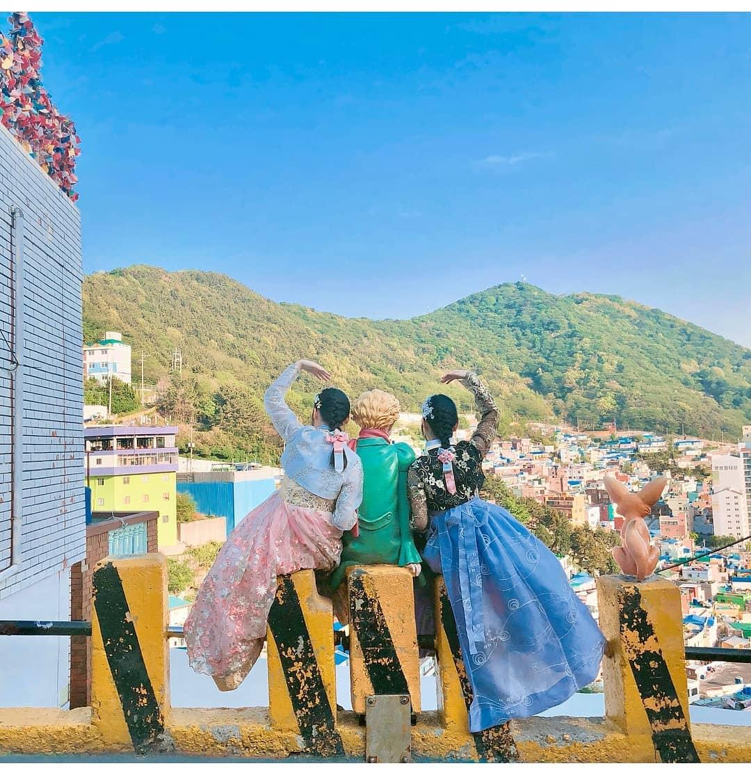 A group of happy people in traditional Korean clothes at a rental store overlooking azure mountains, enjoying leisurely travel.