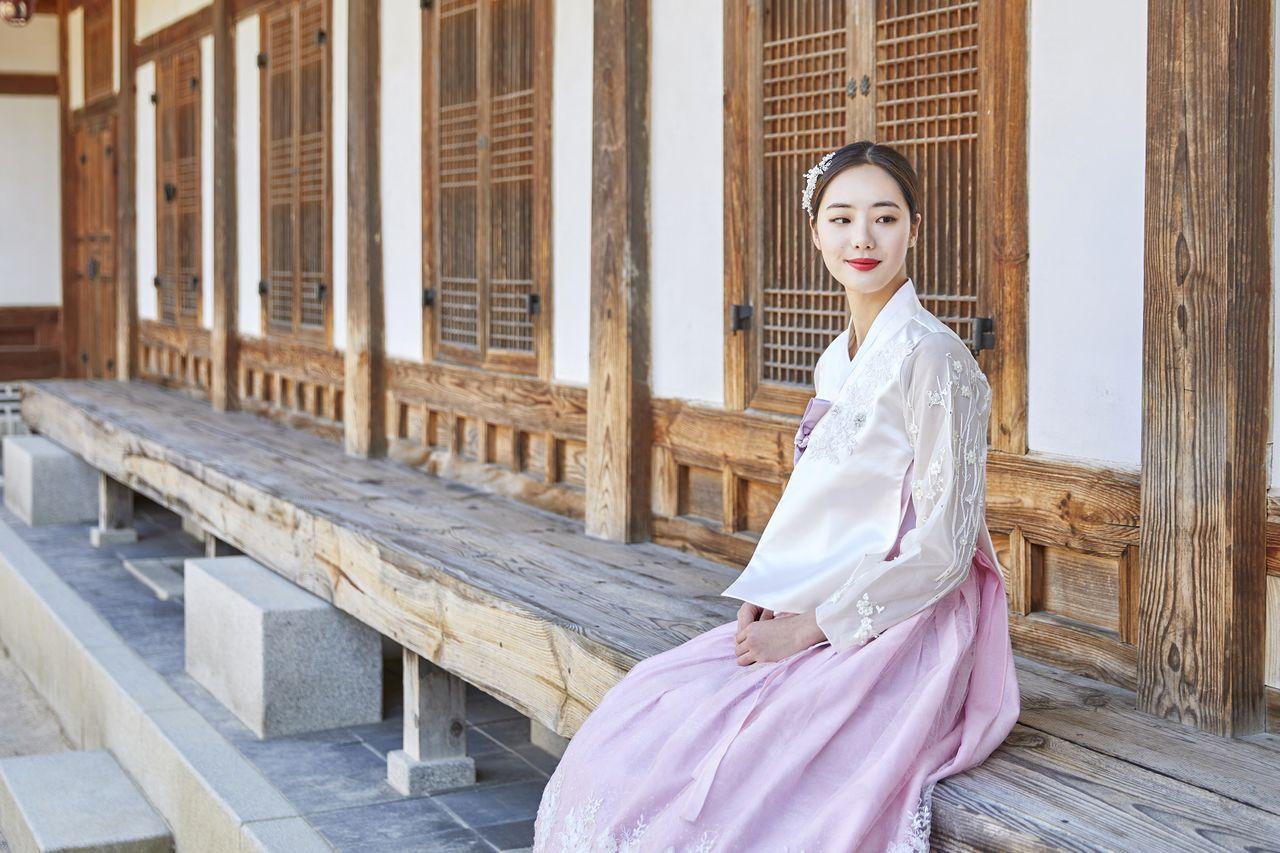 A woman wearing Korean traditional clothing standing in a temple courtyard posing for a photo.