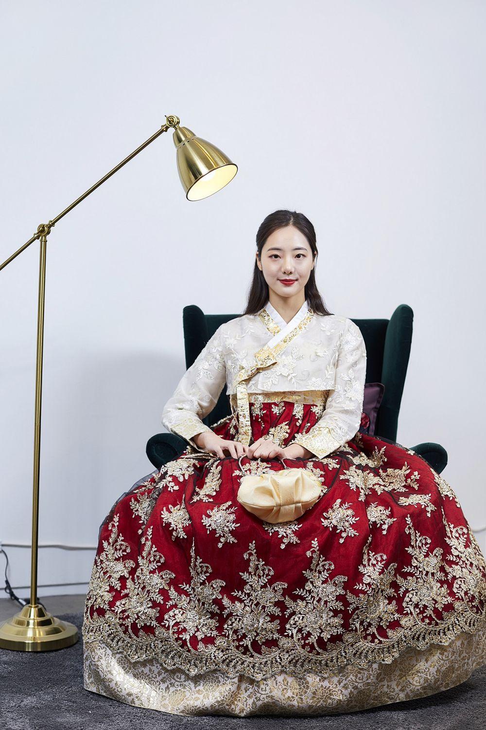 A woman wearing a traditional Korean gown with embellishments, smiling and looking at the camera.